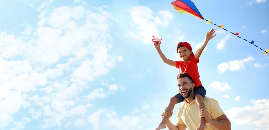 A dad flies a kite with his son sitting on his shoulders.